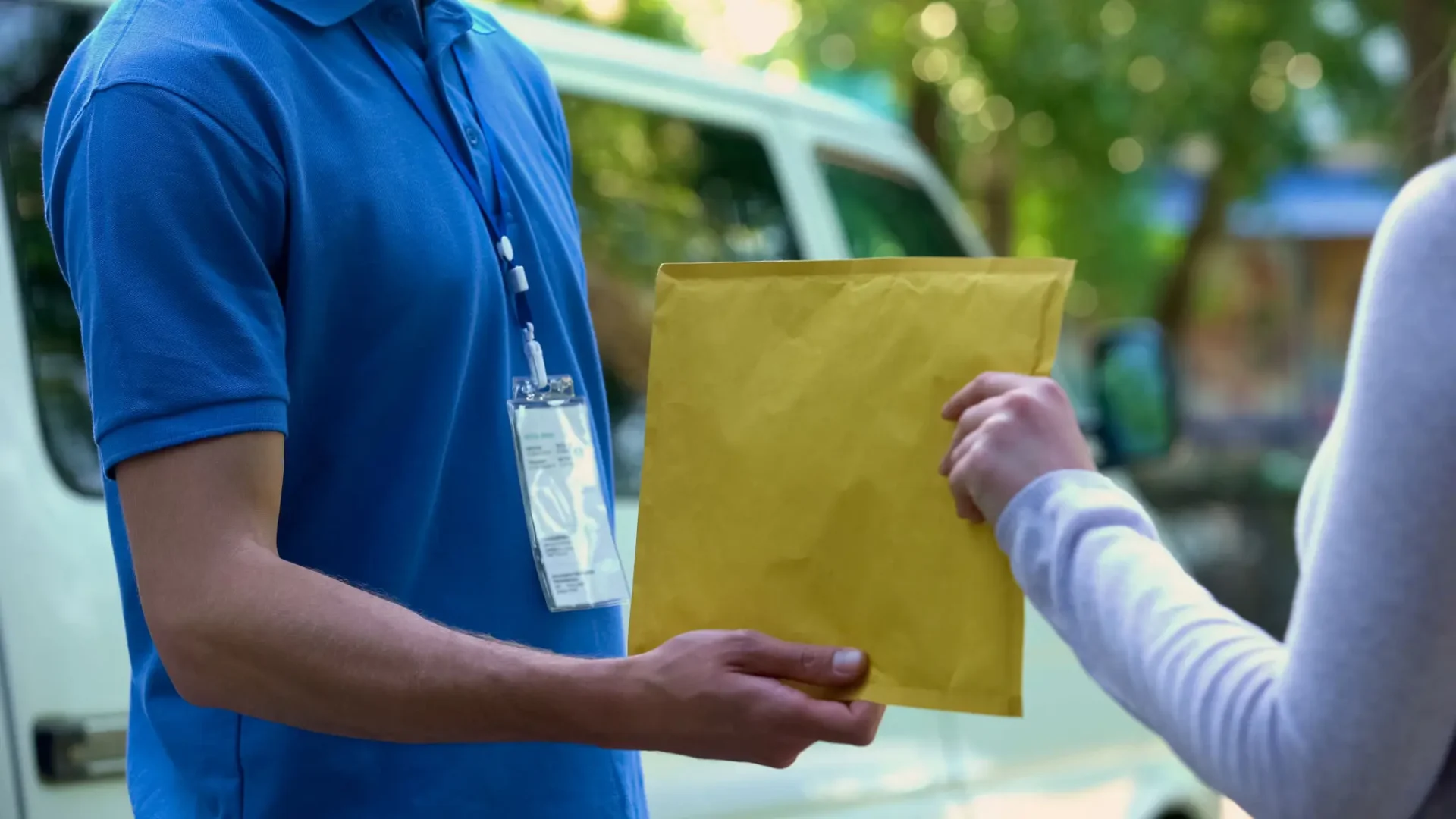 Two people exchanging a large yellow envelope outdoors.